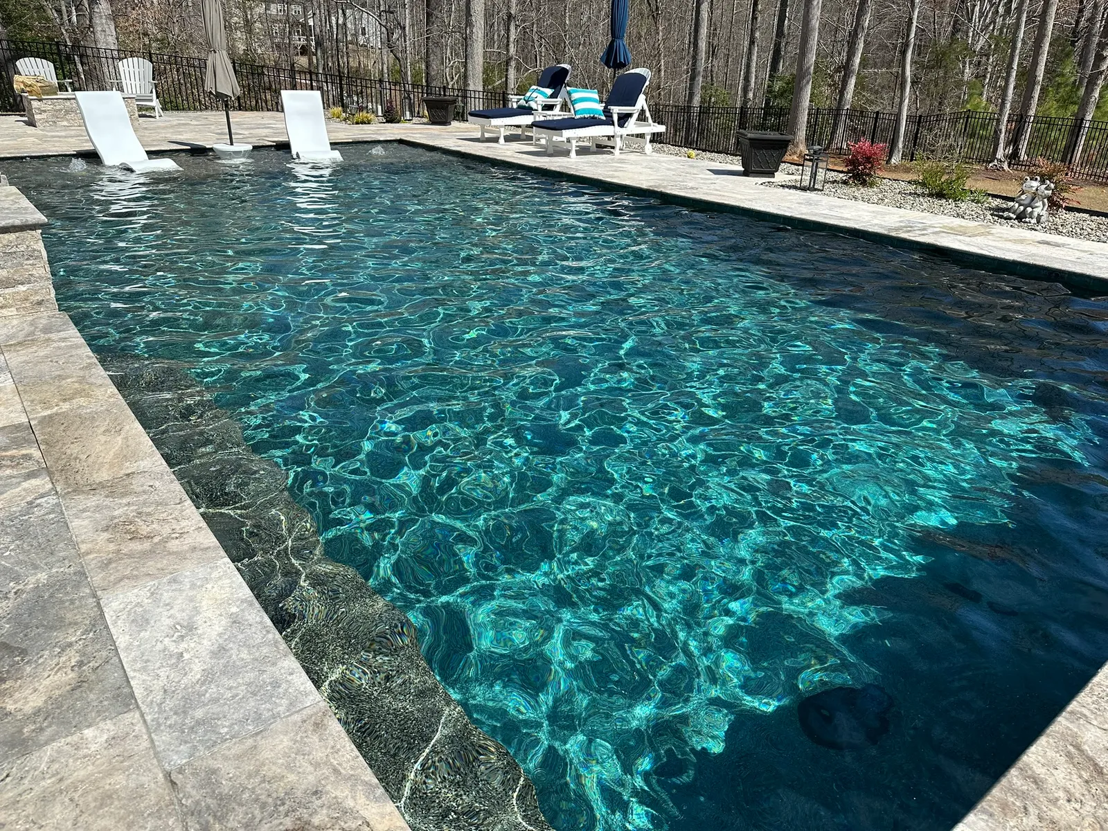 A crystal-clear residential pool with a tanning ledge, maintained by The Pool Collective