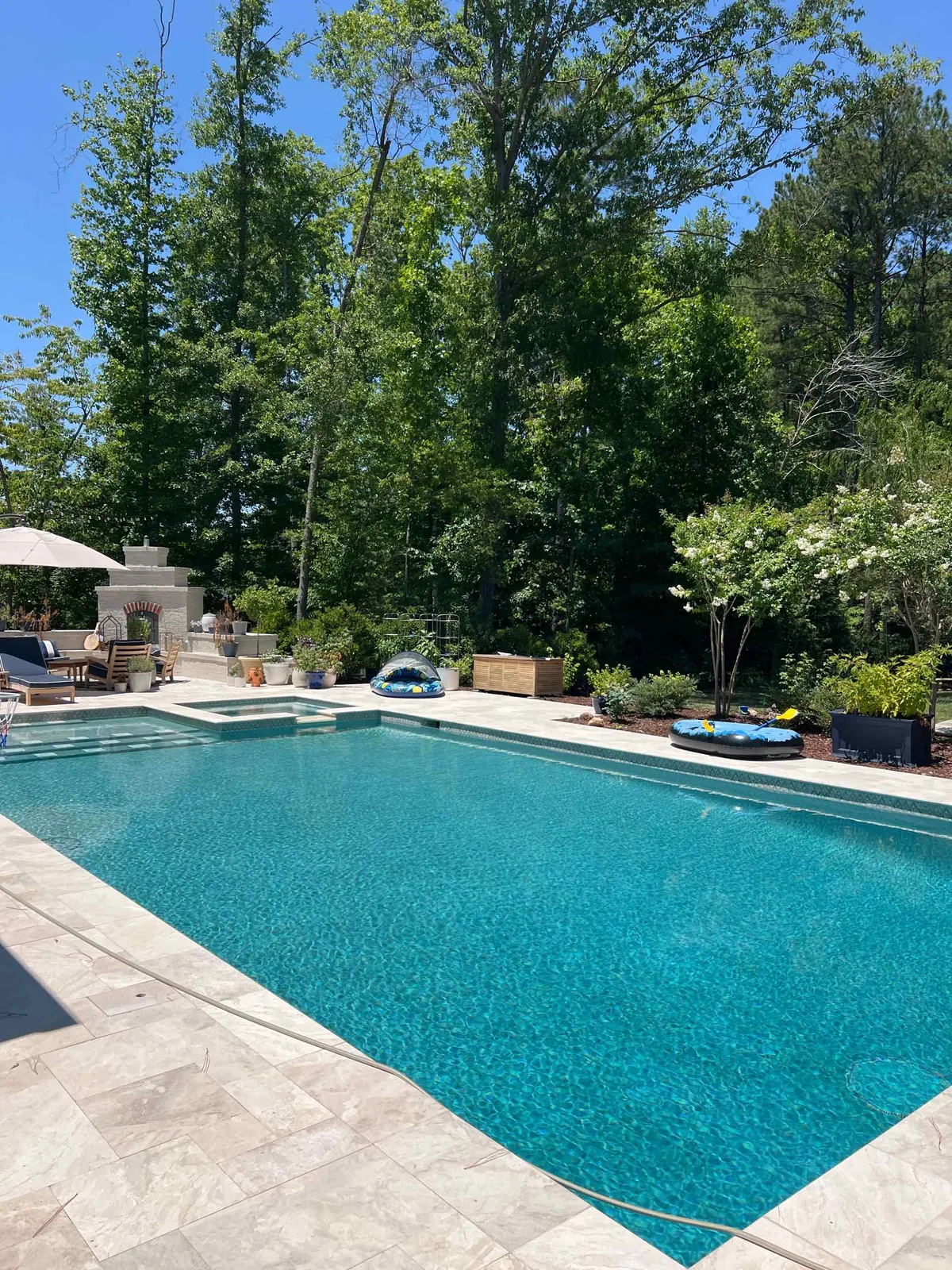 A backyard pool and spa with an outdoor fireplace, ready for neighbors to enjoy